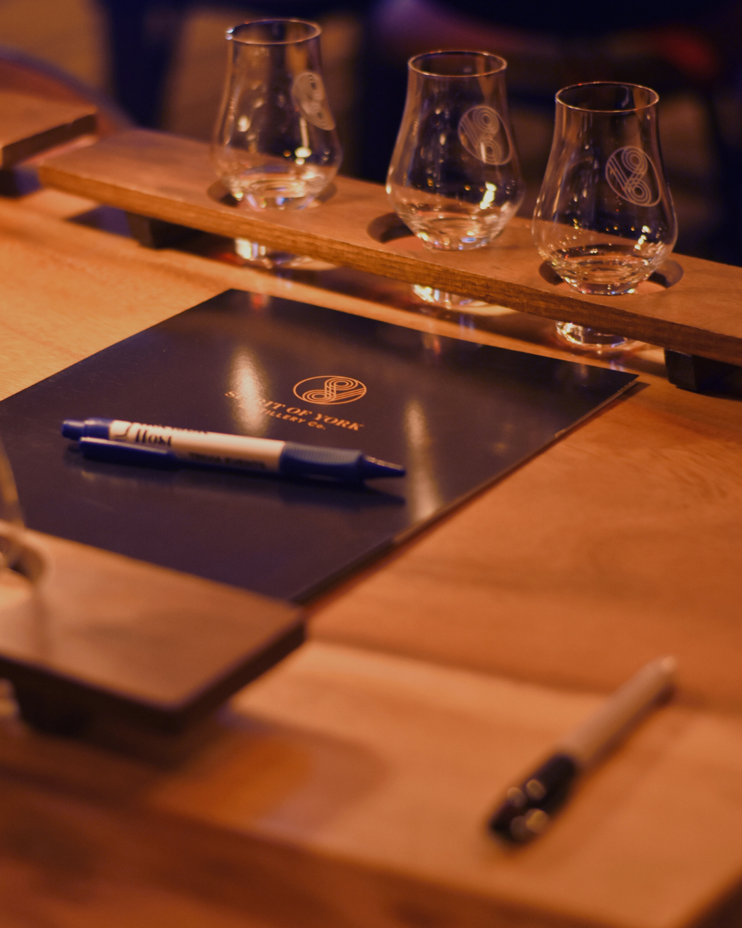 Three empty glasses on a wooden stand with a folder and pen on a wooden table.